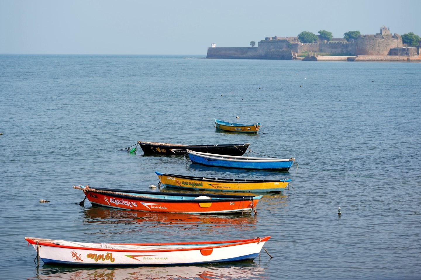 Colourful fishing boats moored in the sea with Diu Fort on the horizon