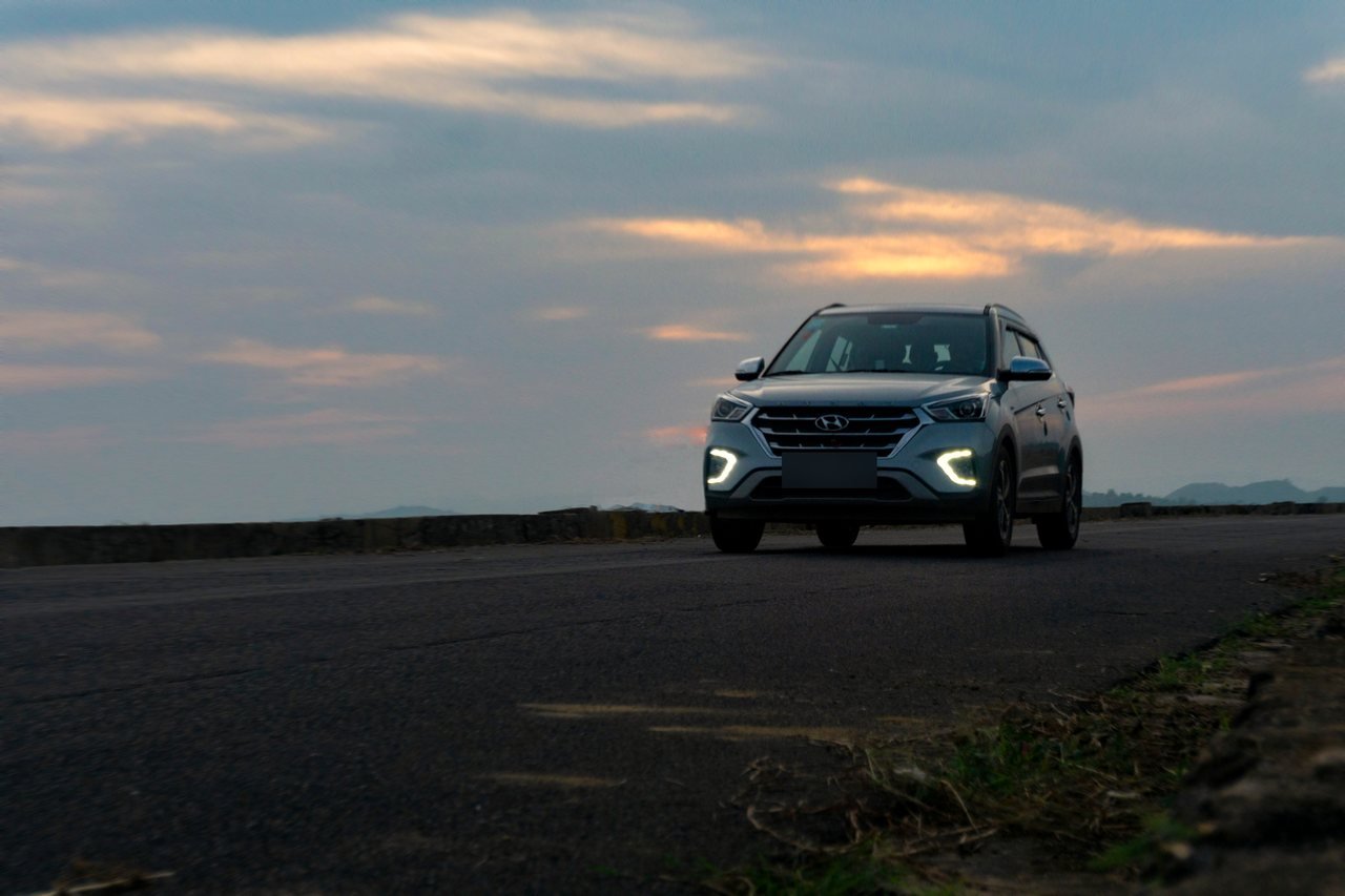 SUV with its daytime lights on, waiting on an open highway under a dusk sky