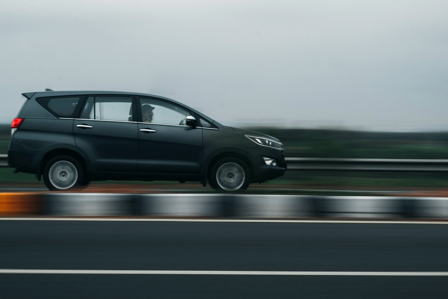 Grey Toyota Innova Crysta speeding along a highway, the guardrail blurred behind it
